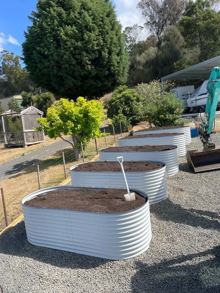 Raised corrugated garden beds installed on gravel with excavator on site