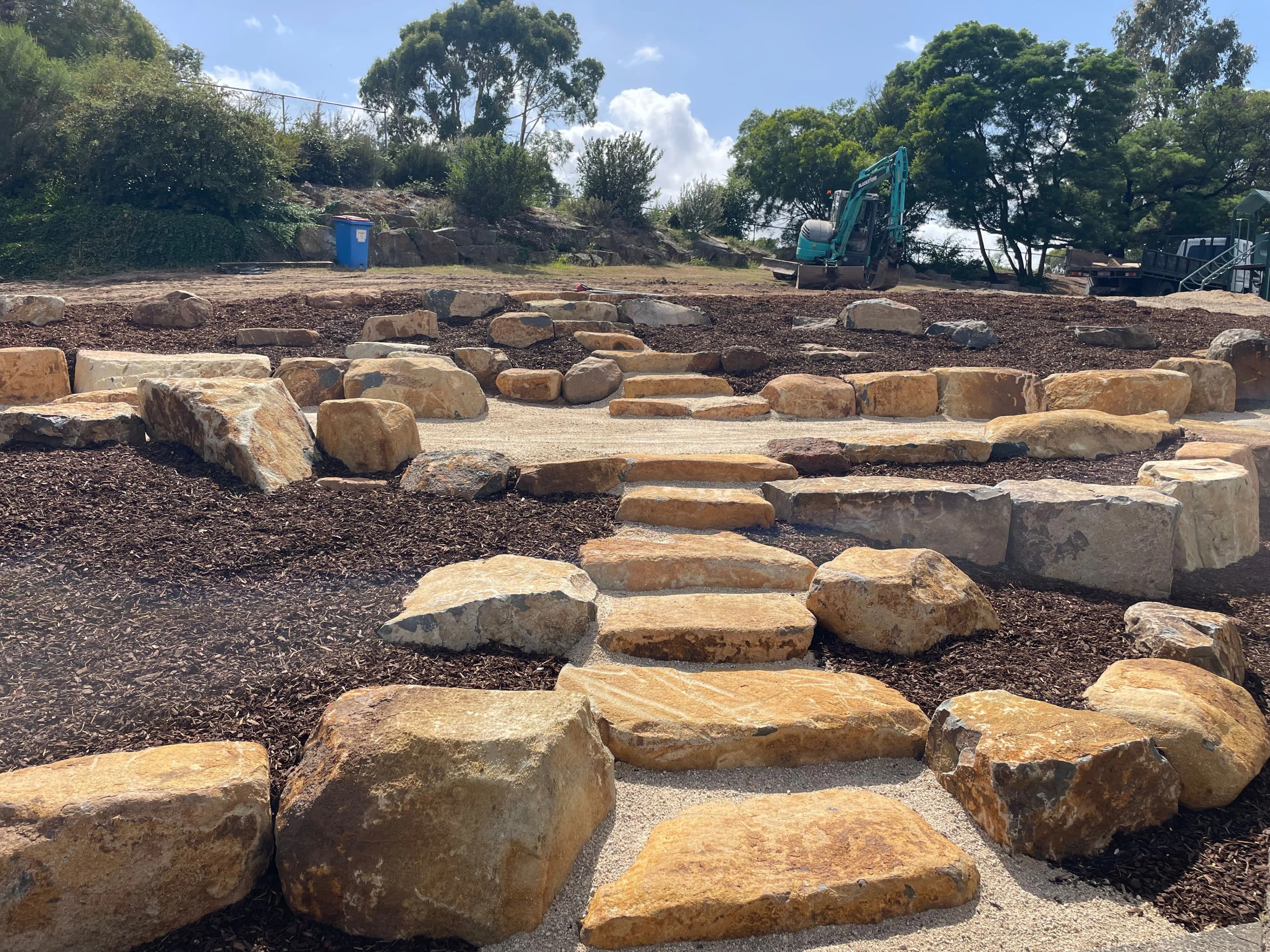 Sandstone steps and terraced landscaping under construction with excavator on site