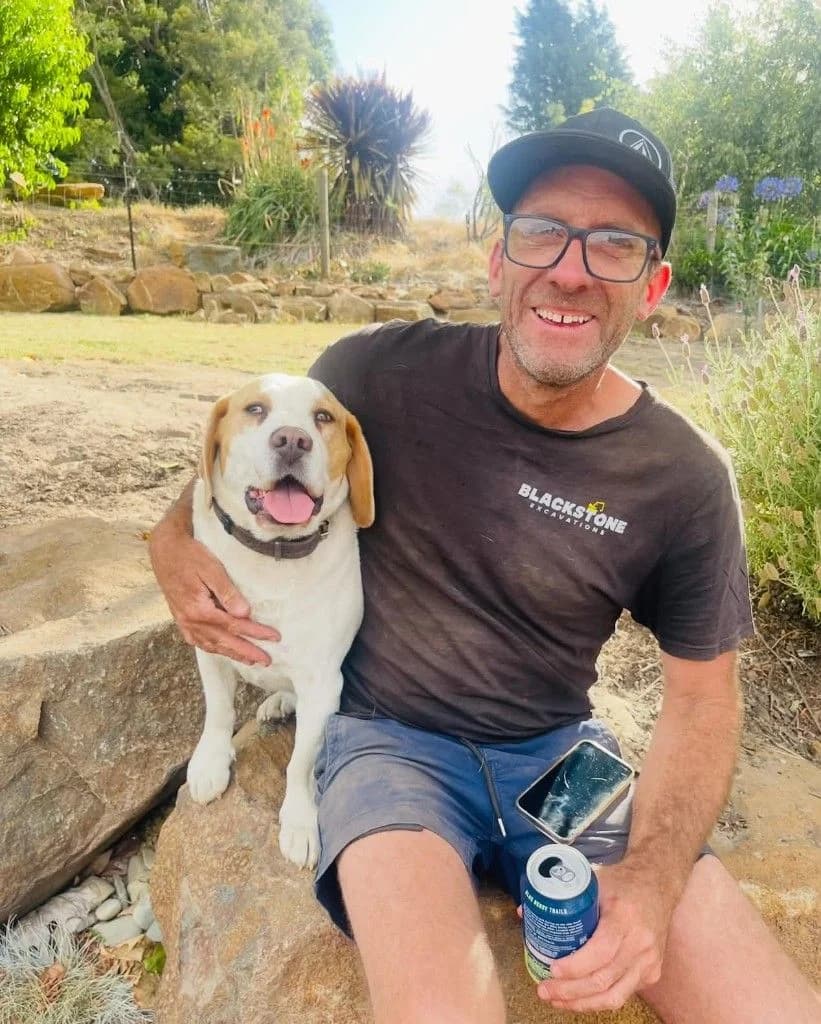 The owner of Blackstone Excavations smiling outdoors with his dog, wearing a branded company shirt.
