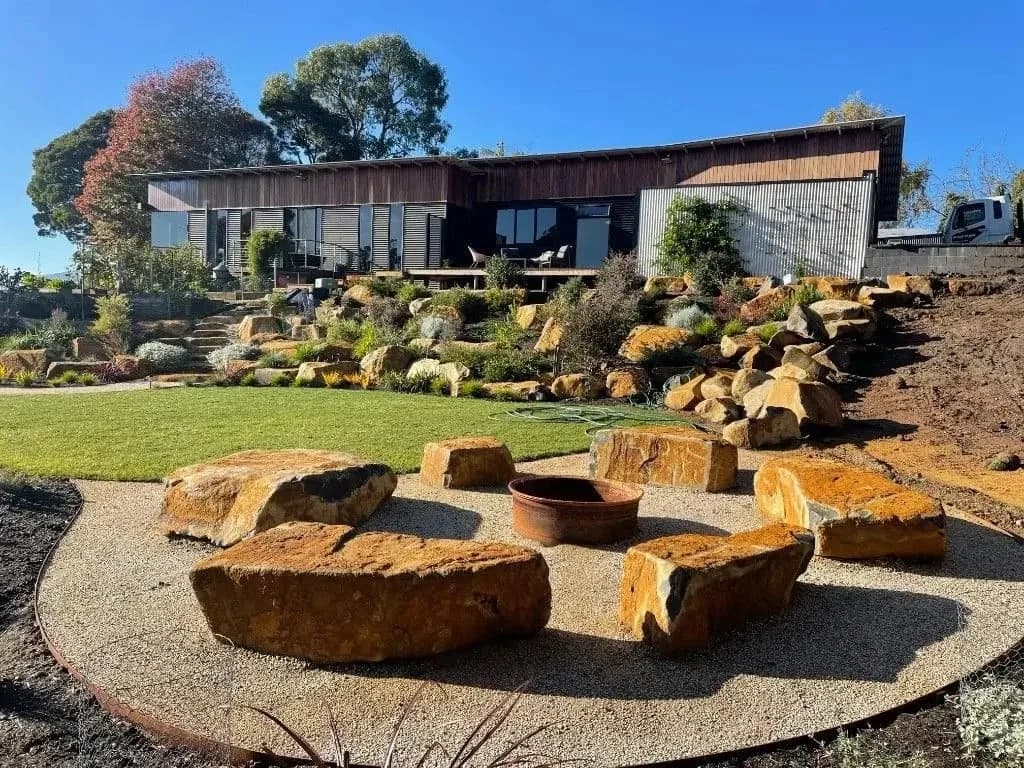 Backyard rock landscaping with fire pit, tiered stone garden, and modern home